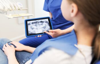 people, medicine, stomatology, technology and health care concept - close up of female dentist showing teeth x-ray on tablet pc computer screen to patient girl at dental clinic office